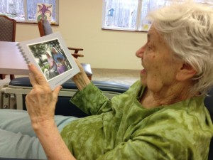 Shirley is in her recliner smiling as she gazes upon a photo of herself from 2003.