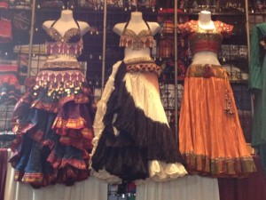 A costume vendor displays authentic belly dancing garb on manikins suspended from an overhead beam.