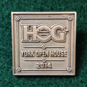 In photo. The pin is a square piece of metal the color of puter. On it are the words "HOG: York Open House. 2014" End photo.