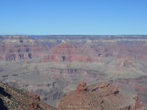 In photo. Looking north at the southern rim of the Grand Canyon. Layers of color can be seen as the canyon walls extend from the canyon floor up to the horizon. End photo.