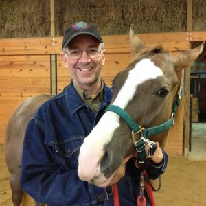 In quintessential portrait fashion, I am standing and smiling for the camera while a large saddled horse allows me to hold her reins. The horse's head is over my left shoulder and seems quite practiced at this business of mugging for the camera.