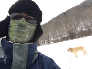 In photo -- Ed is seen in a selfie pose with Ryder on flexileash in the distance behind him. But you wouldn't really know it was Ed because he looks rather like a bandit with a neck-gator pulled up around his face. Dark sunglasses cover his eyes and a fur hat is pulled down over his ears. Actually, his ski jacket is very recognizable as it is the one he has worn every year for the past 10 or more years. Out of photo.