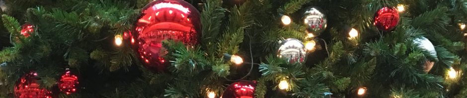 In Photo: Close up of Christmas tree and decorations consisting of Large red globes, white globes, and pine cones. Out of Photo.