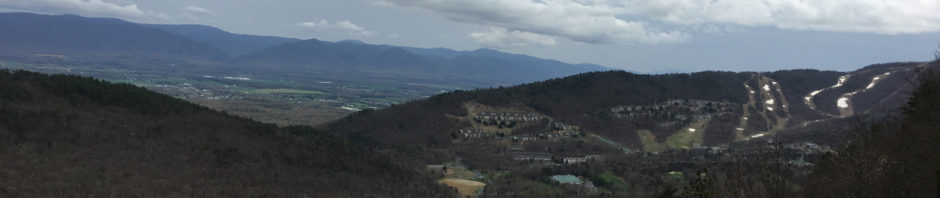 The photo shows three distinct layers of clouds. The distant mountains are partially obscured by a haze. But the nearer mountain and valley are clear. On these near mountainsides, one can see the ski slopes with only patches of stubborn snow not willing to recess in spite of daytime temperatures in the upper 60's.